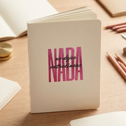 Libreta_A5_No_Dejes_Nada_Entrelineas parada sobre una mesa de madera y con lapices en los lados
