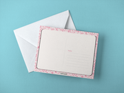 parte de atras de postcard encima de sobre blanco con fondo azul. tarjeta con frase "mama ser tu hijo es mi trauma favorito"