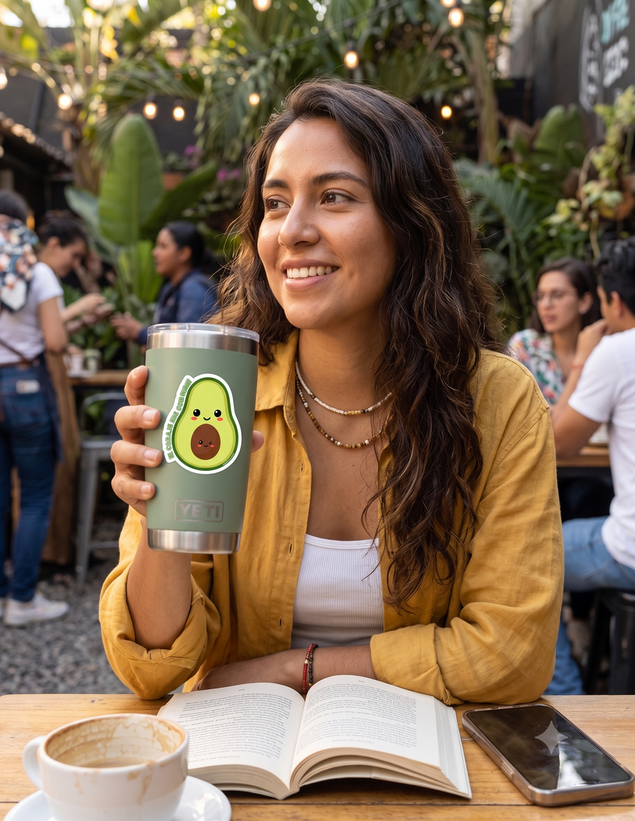 joven latina, sonríe mientras sostiene un tumbler Yeti de color verde en la mano derecha. El tumbler tiene pegado el stickler de aguacate sonriente con la frase El Coraje Me Consume.