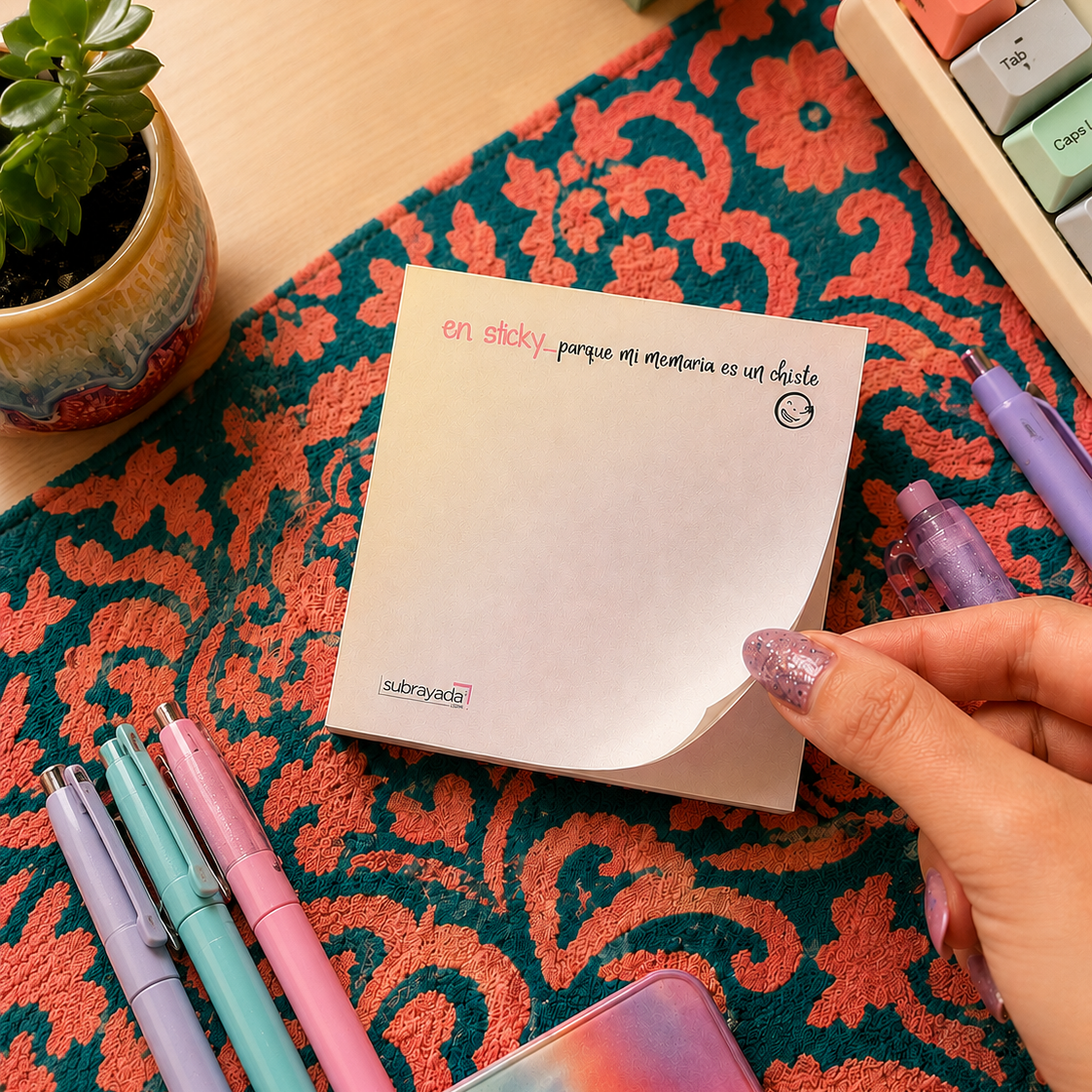 woman's hand tearing a note from the sticky notes pad that has the phrase "en sticky... porque mi memoria es un chiste 😂"