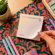 woman's hand tearing a note from the sticky notes pad that has the phrase "en sticky... porque mi memoria es un chiste 😂"